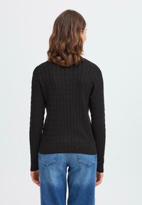 Pull en maille noir texturé avec une silhouette ajustée et des manches longues, associé à un jean en denim bleu clair.