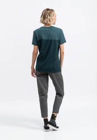 Teal T-shirt met korte mouwen en een gelaagd ontwerp, gecombineerd met grijze broeken. De outfit wordt aangevuld met zwart-witte sneakers.