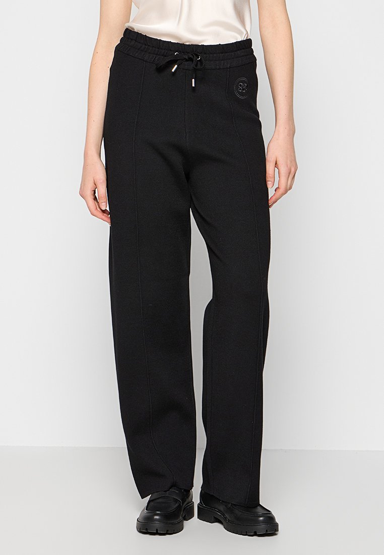 Schwarze Sweatpants aus weichem Stoff, mit einem Kordelzugbund, seitlichen Nähdetails und einem runden Logo auf dem linken Oberschenkel.