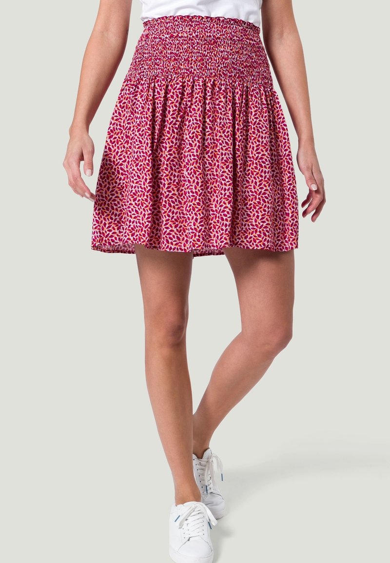 Falda con cintura fruncida y silueta acampanada, que presenta un patrón de hojas en rosa y blanco sobre una tela ligera. Combinada con zapatillas blancas.