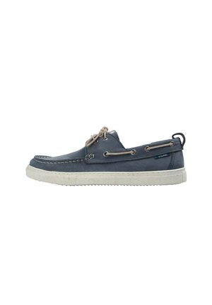 Zapato náutico de cuero azul marino con cordones beige, suela de goma blanca, ojales laterales y tira para tirar en el talón.