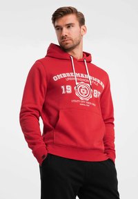 Röd hoodie i bomullsmix. Har känguruficka, dragsko på huvan och vittryckt design med text och grafik. Ribbad mudd och nederkant.