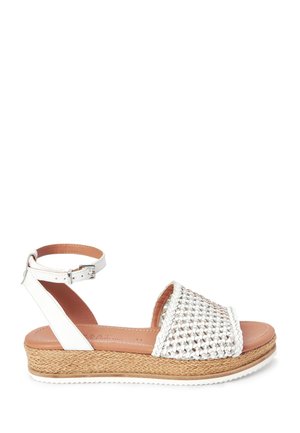 White woven sandals featuring a braided upper and ankle strap, with a thick woven espadrille sole and a smooth leather insole.