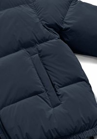 Sezione di giacca imbottita blu navy che mostra il tessuto trapuntato, la tasca diagonale cucita e parte della manica.