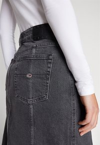 Grå denimkjol med hög midja, med ett svart märkesband i midjan, bakfickor och en klassisk rak modell.