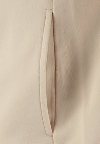 Tessuto di abbigliamento beige con una superficie texture, caratterizzato da una cucitura verticale e una piccola tasca integrata con un'apertura stretta.