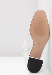 Chaussure blanche à talon bloc, tige en cuir lisse et bout arrondi. Comprend un détail de fermeture éclair et une semelle en caoutchouc texturée. Taille 37.