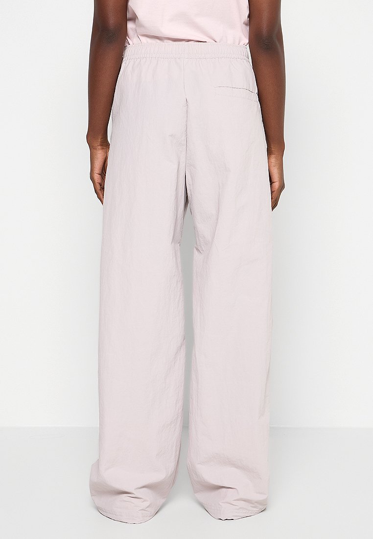 Pantalons larges rose clair en tissu texturé. Dotés d'une taille élastique et d'une poche arrière. Design fluide et élégant.