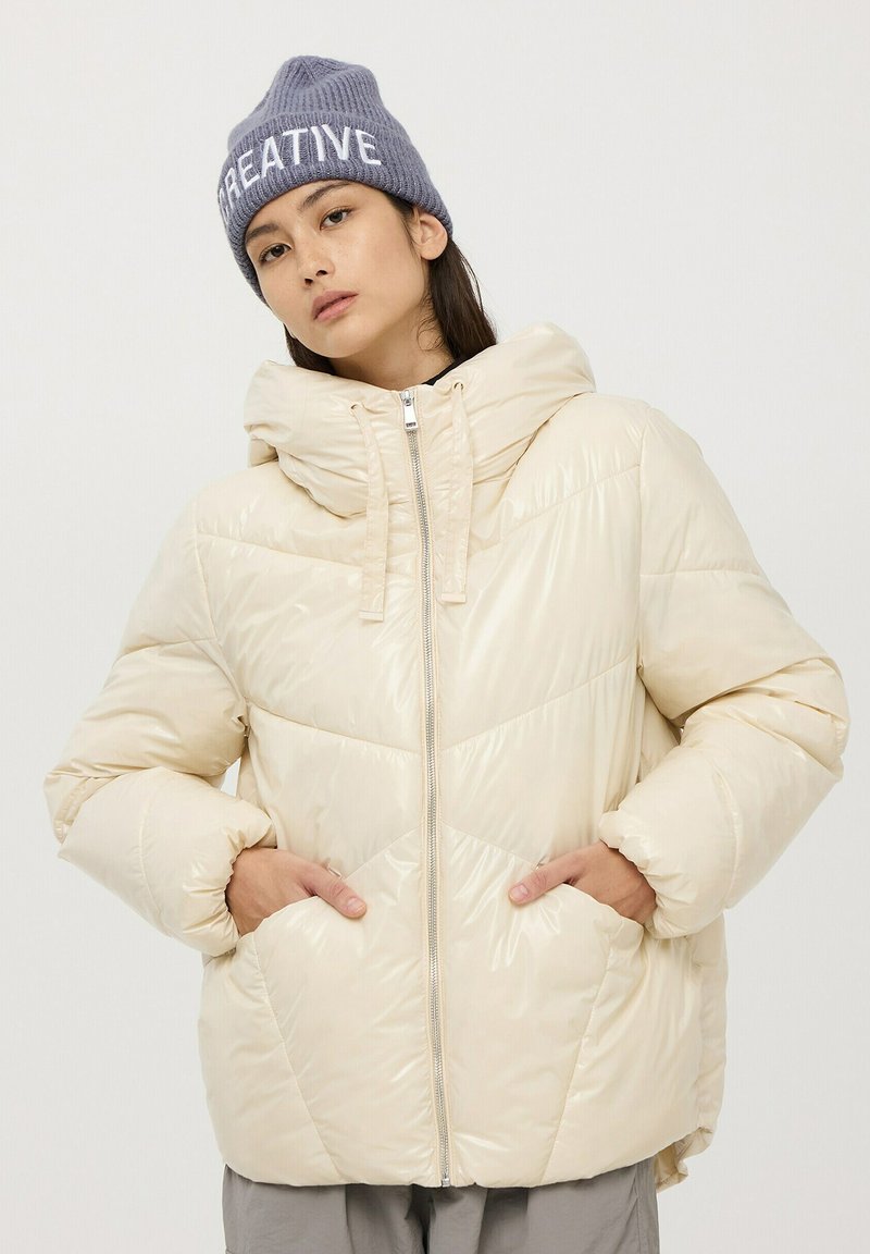 Puchowa, kremowa kurtka z kapturem, z zapięciem na zamek i ukośnymi przeszyciami. Szara czapka z prążkowanym wykończeniem z białym napisem "CREATIVE".