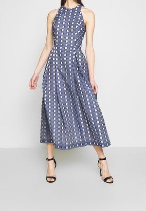 Marineblauwe jurk met een halterhals, voorzien van een rasterpatroon van witte en lichtblauwe vierkanten, met een vloeiende silhouet en een lengte tot halverwege de kuit.
