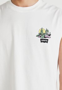 Fehér, ujjatlan pamut póló színes kaktusz grafikával és napmintával, amely a fekete "Levi's" logó fölött található az elején.