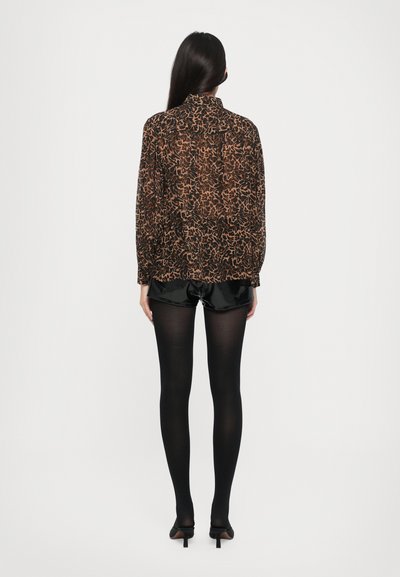 Sort og brun mønstret gennemsigtig bluse med høj krave og lange ærmer, parret med sorte satin shorts og sorte strømpebukser, båret med spidse hæle.