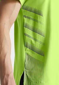 Camiseta deportiva verde lima con detalles de patrón en zigzag y puntos en gris oscuro a los lados, hecha de material ligero y transpirable.