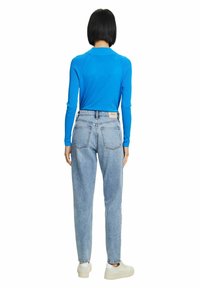 Maglietta azzurra a maniche lunghe con un design aderente; jeans a vita alta azzurri chiari con una vestibilità comoda e tasche posteriori; sneakers bianche.