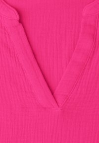 Lyserødt tekstureret stof med et foldet V-formet halsudskæringsdetalje på et beklædningsgenstand.