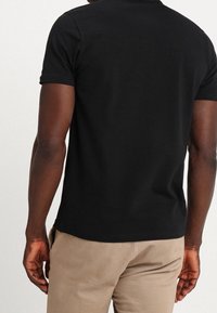 T-shirt noir à manches courtes en coton. Design ajusté avec un col rond, présentant une texture lisse et un style minimaliste.