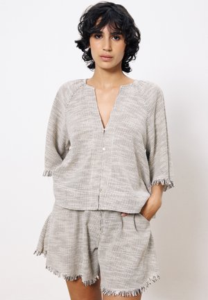 Beige en crèmekleurig gebloemd shirt met een V-hals en korte mouwen, gecombineerd met bijpassende shorts met franjes aan de randen en zijzakken.