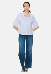 Camicia a maniche corte a righe azzurre con due tasche sul petto, abbinata a jeans in denim scuri a gamba larga e ballerine argento metallico.