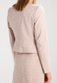 Blazer tailored di un rosa chiaro con un motivo floreale testurizzato, maniche lunghe e design aderente. Presenta un orlo dritto e una cucitura sul retro.