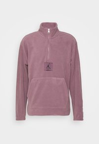 Fleecepullover i ljuslila med halv dragkedja, sidfickor och en svart Jordan-logopatch på framsidan. Mjuk textur.