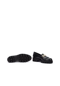 Mocasines de cuero negro con suela gruesa, que presentan una cadena decorativa dorada y detalles de flecos. La suela exterior tiene textura para mayor agarre.