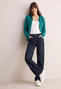 Turquoise cardigan met een capuchon, knoopdetails, over een wit tanktop; gecombineerd met donker denim jeans en witte sneakers. Gladde textuur overal.