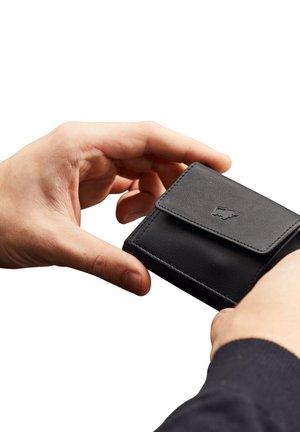 Schwarze Lederbrieftasche, die in einer Hand gehalten wird, mit einem Klappverschluss, gesteppten Kanten und einem kleinen, eingeprägten Logo auf der Vorderseite.