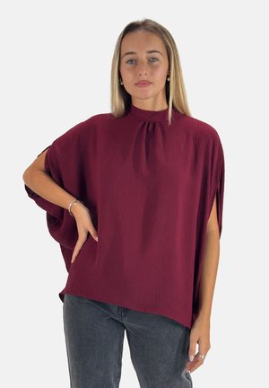 Haut en crêpe bourgogne avec un col haut et des manches amples ; tissu texturé ; coupe décontractée ; associé à un jean en denim sombre.