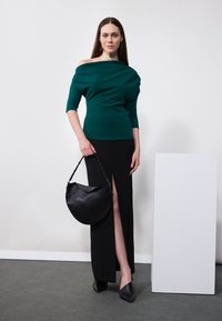 Grønn off-shoulder topp, svart skjørt med sidesliss, svart håndveske med buet form, og svarte spiss-sko. Glatte teksturer.