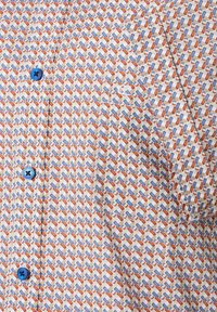 Kurzärmliges gemustertes Hemd in Creme mit geometrischem Design in Blau, Orange und Weiß. Mit blauen Knöpfen und einer Brusttasche.