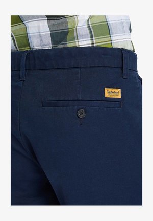 Pantalones azul marino de tela suave que cuentan con un bolsillo trasero con botón y una pequeña etiqueta de Timberland en naranja. Diseño limpio y ajustado sin patrones.