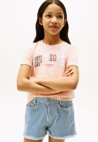 Lys rosa bomulds t-shirt med "HILFIGER" grafik. Kombineret med blå og hvide stribede denimshorts med frynset kant og to lommer.