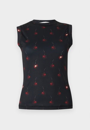 Kvinde står med den ene arm holdende i modsatte albue, iført sort ærmeløs top med røde blomstertryk, mørkt skørt og sorte hæle.