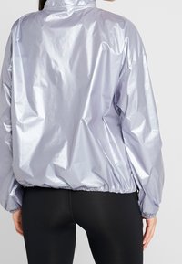 Leichte, reflektierende lavenderfarbene Jacke mit hohem Kragen, elastischen Bündchen und Saum, die eine glatte, glänzende Textur aufweist.