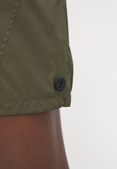 Olive green shorts made of lightweight fabric. Features a black button with the number 7 at the hem. Smooth texture, fitted design.