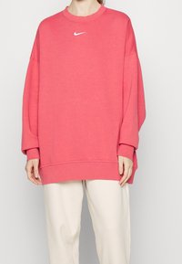 Rosa sweatshirt med en lös passform och oversized design, med en vit Nike-logga på bröstet. Mjuk väv och ribbade ärmmuddar.