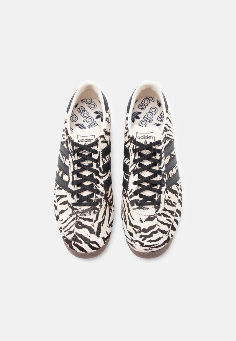 Black and white zebra-striped sneakers with lace-up design, three black stripes, and a textured rubber sole. Logo visible on insole.