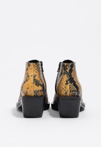 Botas de tobillo con un diseño de estampado de serpiente en tonos marrones y amarillos. Cuentan con un tacón bloque negro y un cierre de cremallera en la parte trasera.