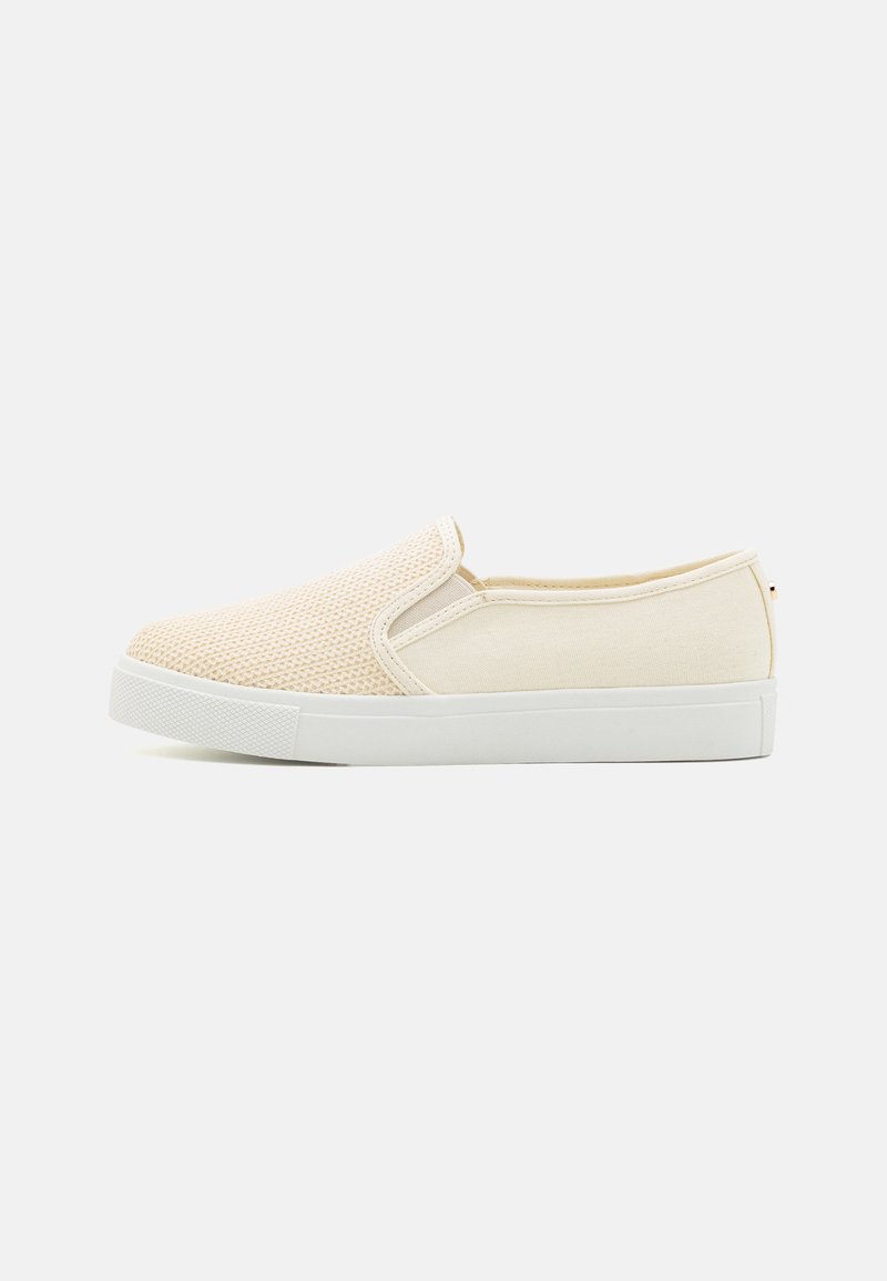 Beige slip-on sko med en pustende mesh-overdel og kanvasdetaljer. Hvit gummisåle med teksturert finish. Minimalistisk design.