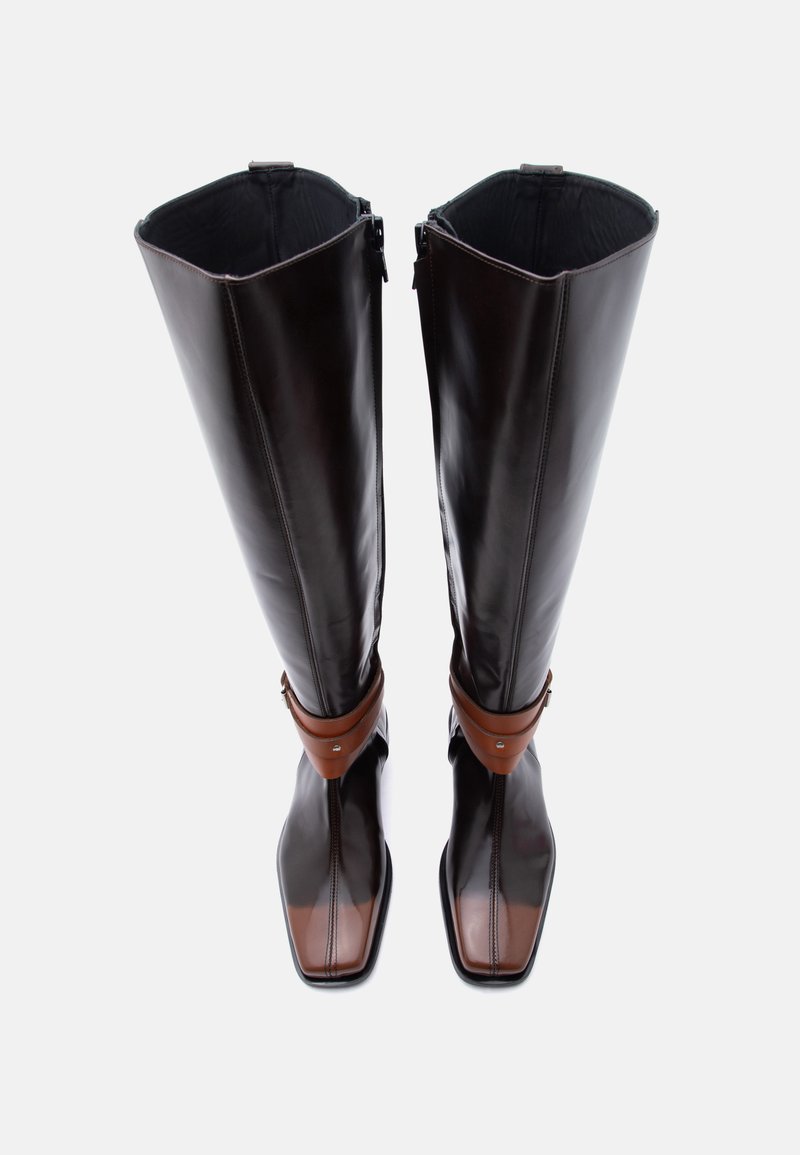 Pair of tall black leather boots with brown toe caps and ankle straps, zip closures on inner sides, square toes.