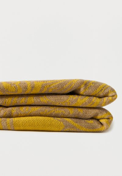 Textile plié brun et jaune à motif, avec un design floral tissé, posé sur un fond blanc uni.