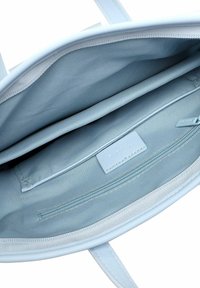 Šviesiai mėlynas rankinės vidus su lygiu audinio pamušalu, turintis užtrauktuko kišenę ir nedidelę etiketę. Matomos dvi atviros kišenės.