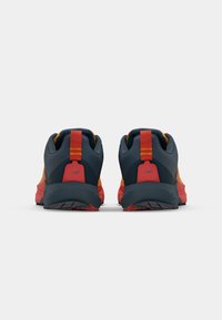Chaussures de course avec une tige en mesh bleu foncé et orange, présentant des accents rouges et un talon texturé, mettant en avant une semelle robuste pour l'adhérence.