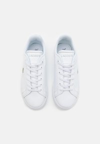 Hvite lær sneakers med en glatt tekstur, rund tå og snørebåndslukking; har grønne logo aksenter på yttersidene.