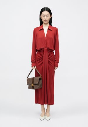 Sarkana kleita ar garām piedurknēm, priekšpusē ar pogām un savāktu auduma detaļu. Komplektēta ar brūnu, teksturētu somu un baltām kurpēm ar smailu purngalu.