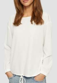 Haut blanc à manches longues avec un motif texturé, encolure arrondie et ourlet à cordon, associé à un short en denim bleu clair.
