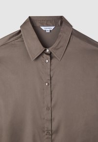 Camicia marrone con colletto a punta, caratterizzata da una texture liscia, bottoni lucidi e un'etichetta che indica la taglia 2XL.