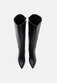 Bottes noires à bout pointu, montantes en cuir lisse avec un design épuré et des accents de fermeture éclair dorée sur le côté extérieur.