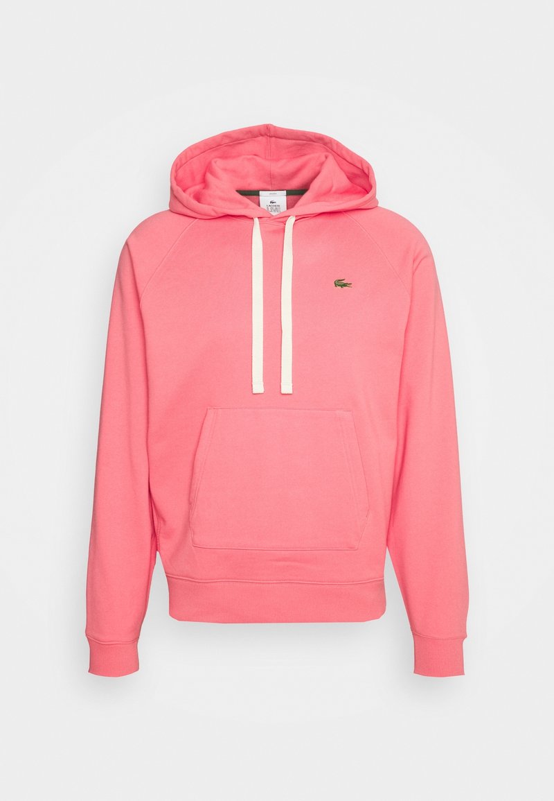 Sweat à capuche rose corail avec poche avant, cordons blancs, poignets côtelés et petit logo crocodile Lacoste vert sur la poitrine.