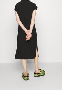 Black knee-length dress with short sleeves and side slit, paired with fuzzy green zebra-pattern slippers.